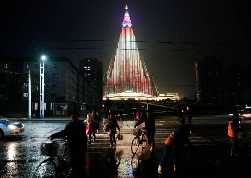 In this Dec. 18, 2018, photo, people cross a street as pyramid-shaped Ryugyong Hotel is seen in the background in Pyongyang, North Korea. Transformed into the backdrop for a gargantuan propaganda display, Pyongyang's yet-to-be-completed 105-story Ryugyong Hotel is once again the talk of North Korea. In a brilliant flip of the script, the uninhabited, pyramid-like building that towers over the North's capital has been festooned with more than 100,000 lights that for several hours every night flash propaganda far and wide. (AP Photo/Dita Alangkara)