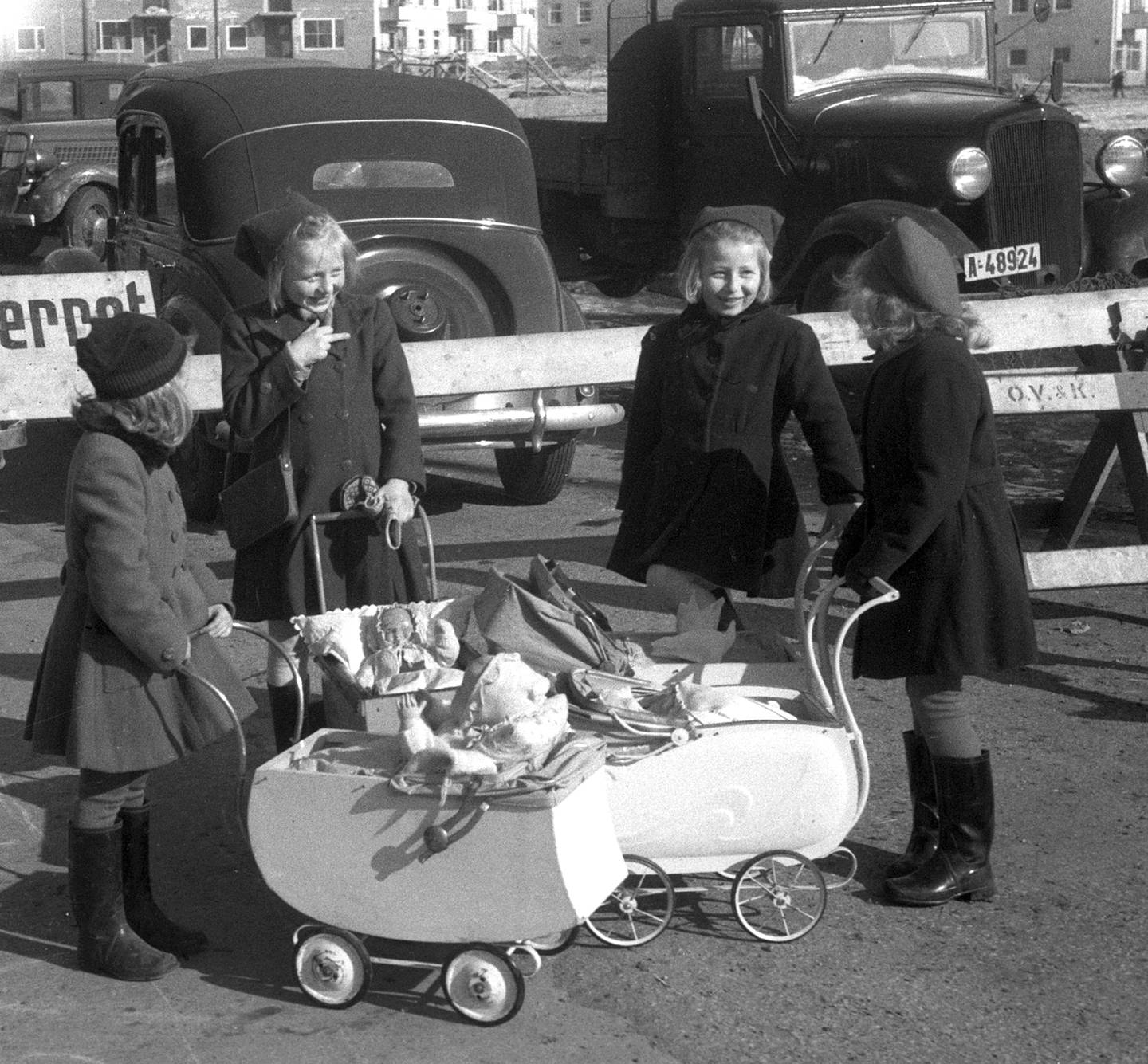 Fire jenter med dokker og dokkevogner, 
mars 1948. Biler i bakgrunnen.