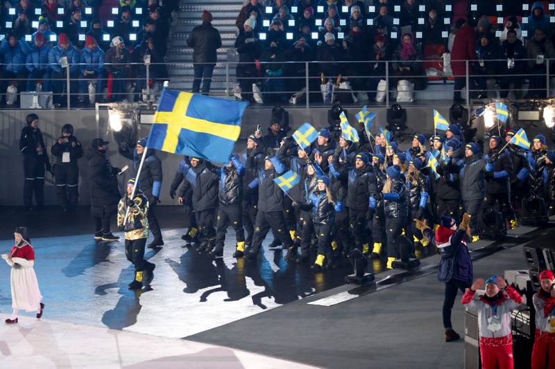 Niklas Edin i gulljakke leder Sveriges trupp inn på arenaen.