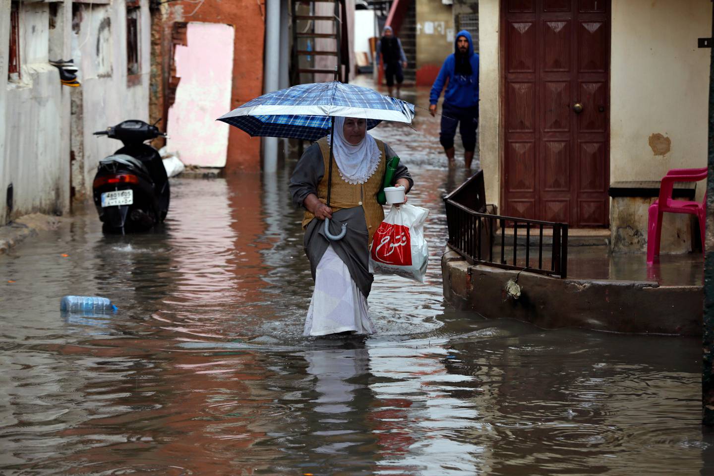 People walk through floodwaters in Beirut's southern suburb of Ouzai, Lebanon, Monday, Dec. 9, 2019. A rainstorm paralyzed parts of Lebanon's capital Beirut on Monday, turning streets to small rivers, stranding motorists inside their vehicles and damaging homes in some areas. (AP Photo/Bilal Hussein)