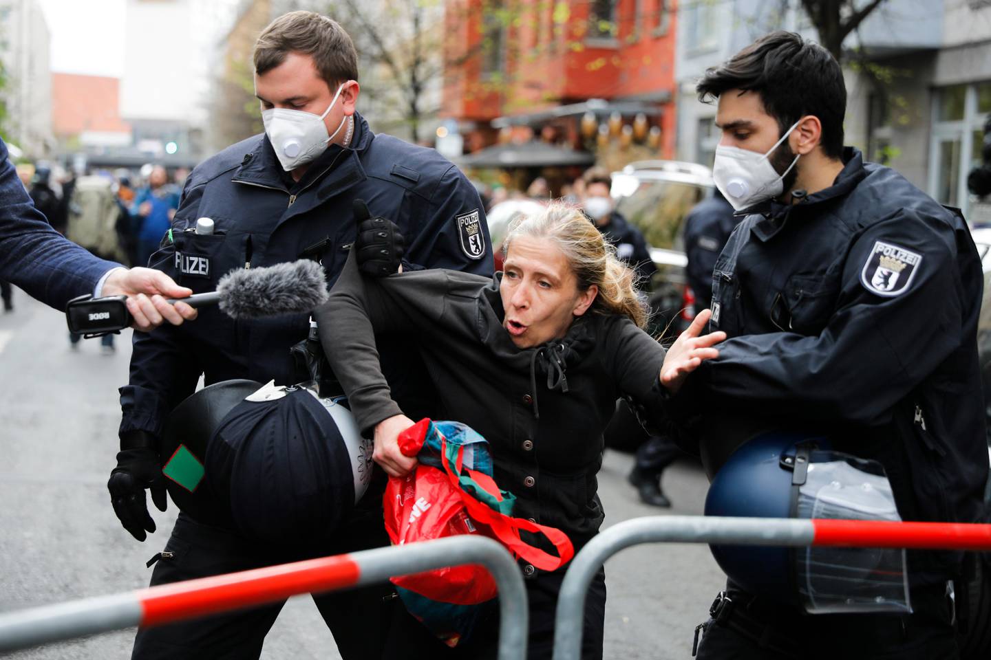 A woman talks to a reporter as she is detain by police officers during an illegal demonstration against the restrictions and measures to prevent the spread of coronavirus in Berlin, Germany, Saturday, April 25, 2020. (AP Photo/Markus Schreiber)