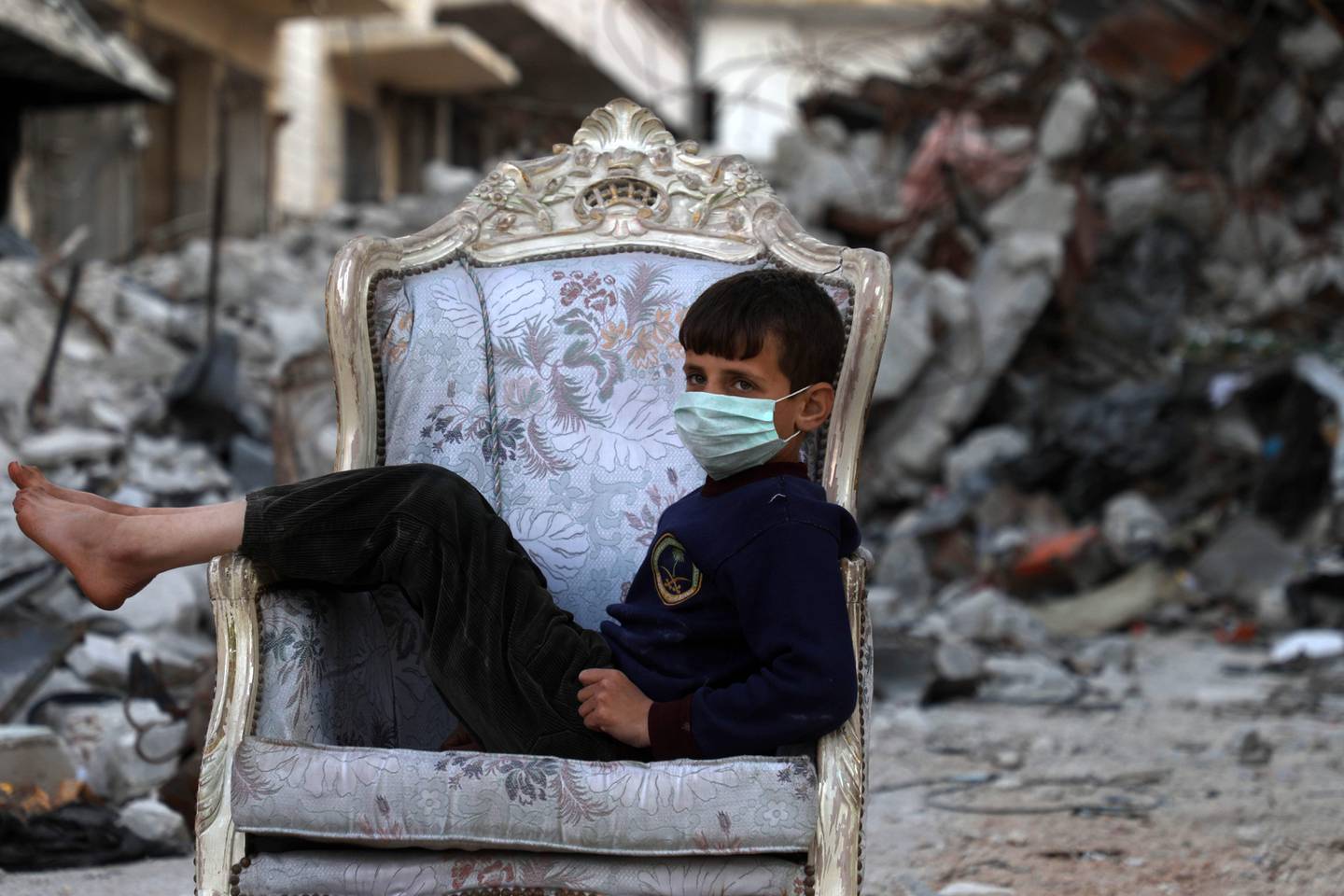 A child sits on a couch found in a street, ravaged by pro-regime forces air strikes, in the town of Ariha in the northern countryside of the Idlib province on April 11, 2020. - Several weeks into a fragile truce that took effect as the novel coronavirus outbreak was turning into a pandemic, hundreds among nearly one million who fled their homes during a deadly regime offensive against the jihadist-dominated region of Idlib  have returned to Ariha, thinking that it is  better than risking their children catch the Covid-19 in  packed displacement camps. (Photo by AAREF WATAD / AFP)