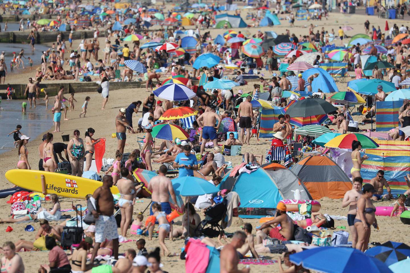 People gather on the beach during hot weather in Bournemouth, southern England, Sunday Aug. 9, 2020. Many Britons are set to bask in another hot day, with clear skies and hot temperatures predicted to continue. (Andrew Matthews/PA via AP)