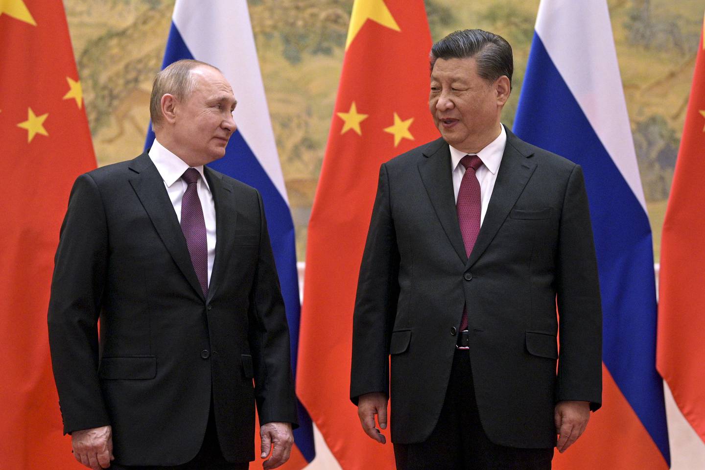 Xi JInping og Vladimir Putin, ser på hverandre, begge stående i svart dress, med slips, foran det russiske og kinesiske flagget.