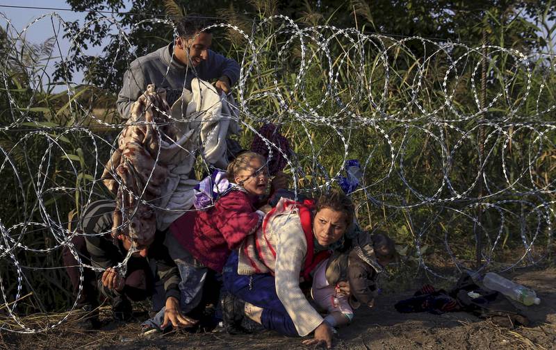 Gjerder: Grensegjerdene er kommet tilbake i Europa for å holde flyktningene ute. Disse syrerne forsøker å krype under piggtråden inn i Ungarn fra Serbia. FOTO: BERNADETT SZABO/NTB SCANPIX