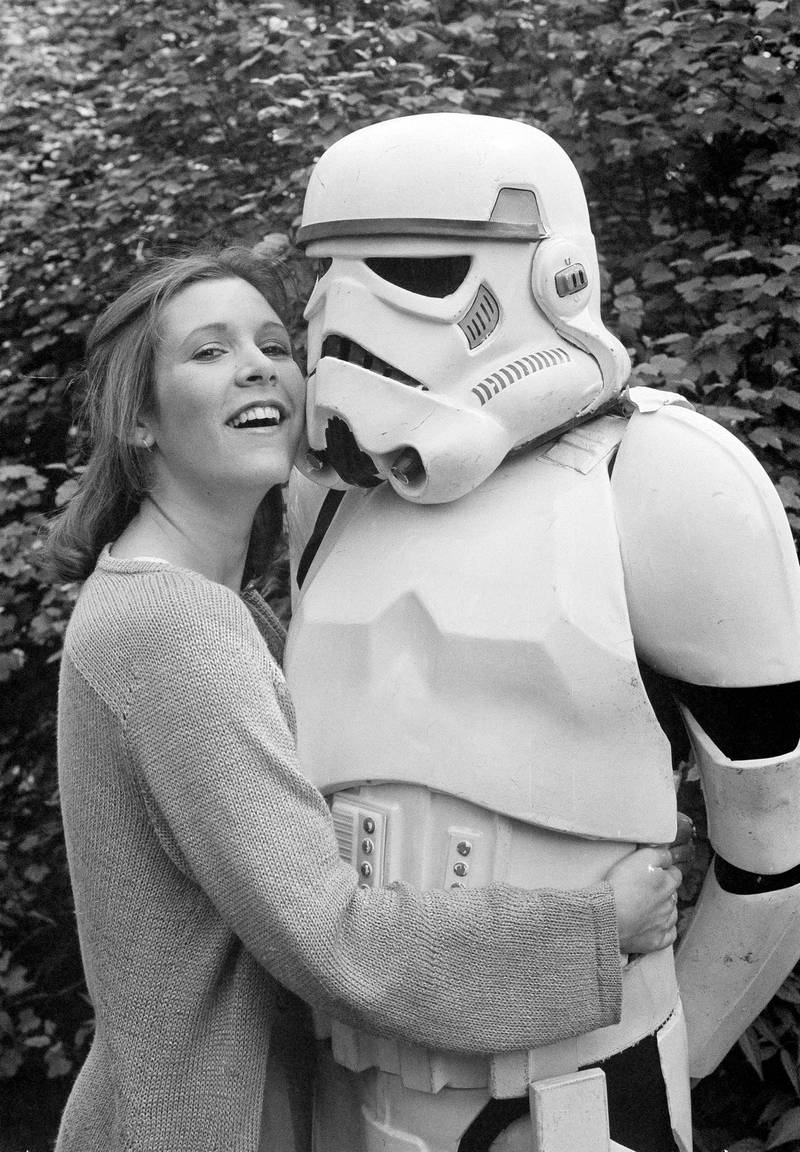 FILE- In this May 23, 1980, file photo, actress Carrie Fisher hugs a person dressed as a stormtrooper in London while promoting the "Star Wars" epic "The Empire Strikes Back." Fisher, a daughter of Hollywood royalty who gained pop-culture fame as Princess Leia in the original "Star Wars" died Tuesday, Dec. 27, 2016. She was 60. (AP Photo/Dave Caulkin, File)