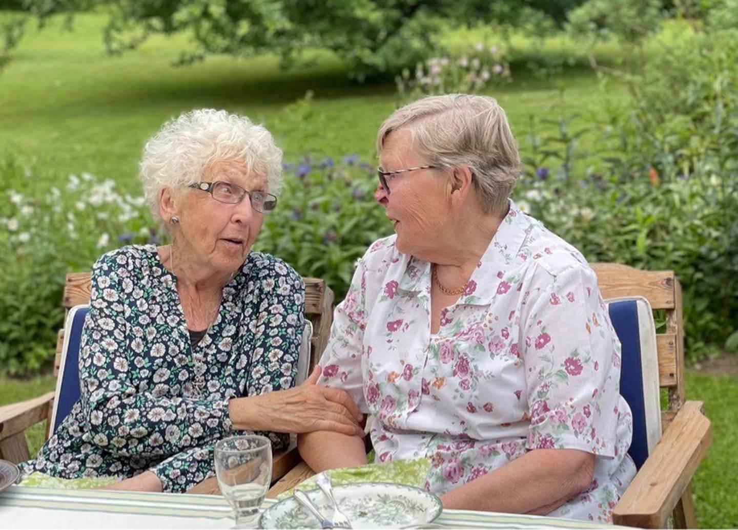 To eldre damer sitter ved siden av hverandre og prater.