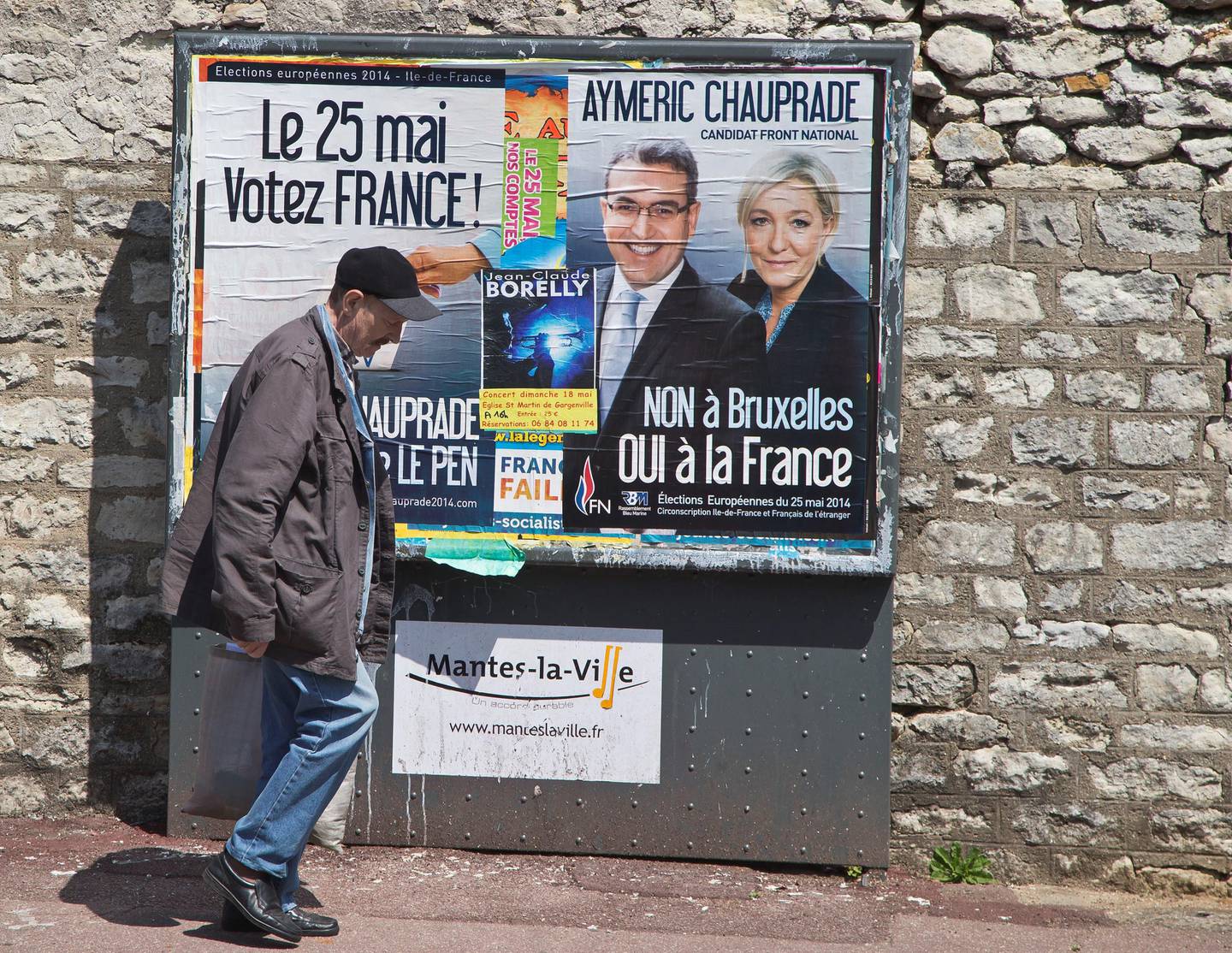 A man walks past campaign posters of the National Front far-right party in Mantes la Ville, north west of Paris, Friday, May 16, 2014. A new mosque for Muslims approved last year and paid with a heavy deposit is suddenly in limbo in a town outside Paris, and new shops in a southern town that reflect Muslims' traditions will be banned. Newly-installed far-right mayors in Mantes-la-Ville, west of the French capital, and in Beaucaire, in southwest France, are rolling out their programs and the large Muslim populations in their towns risk getting crushed. Poster left reads,"May 25 vote for France", poster right, with the pictures of the candidate of National Front far-right party for the European parliament election Aymeric Chauprade  and their leader Marine Le Pen which reads"Brussels No, France Yes". (AP Photo/Michel Euler)