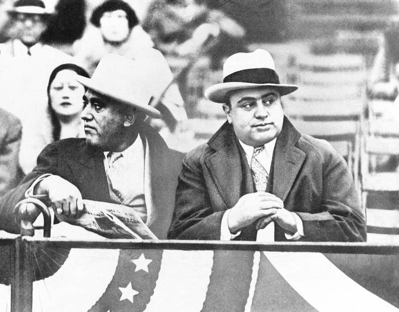 FILE - In this Oct. 10, 1931, file photo Al Capone, Chicago gangland, right, attends a game between Notre Dame and Northwestern Grid in Chicago. Former Alderman A.J. Prignano is on the left. Capone earned tens of millions of dollars annually from bootlegging and speakeasies. (AP Photo, File)