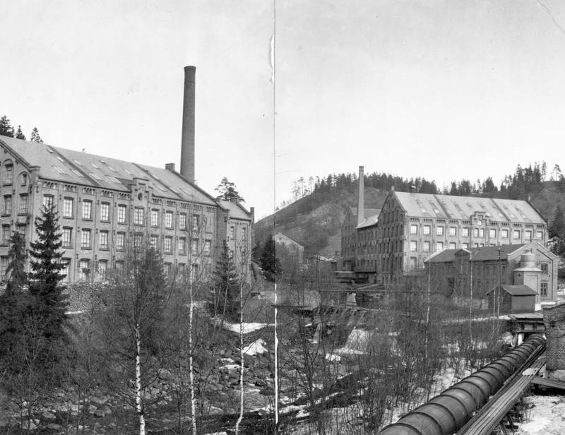 VEVERIENE 1920: «Væveri B» lå på vestsida av elva og «Væveri A» på østsida. Den lave bygningen i forkant er «Ruggeriet» hvor tøystoffene ble viderebehandla til for eksempel flanell.