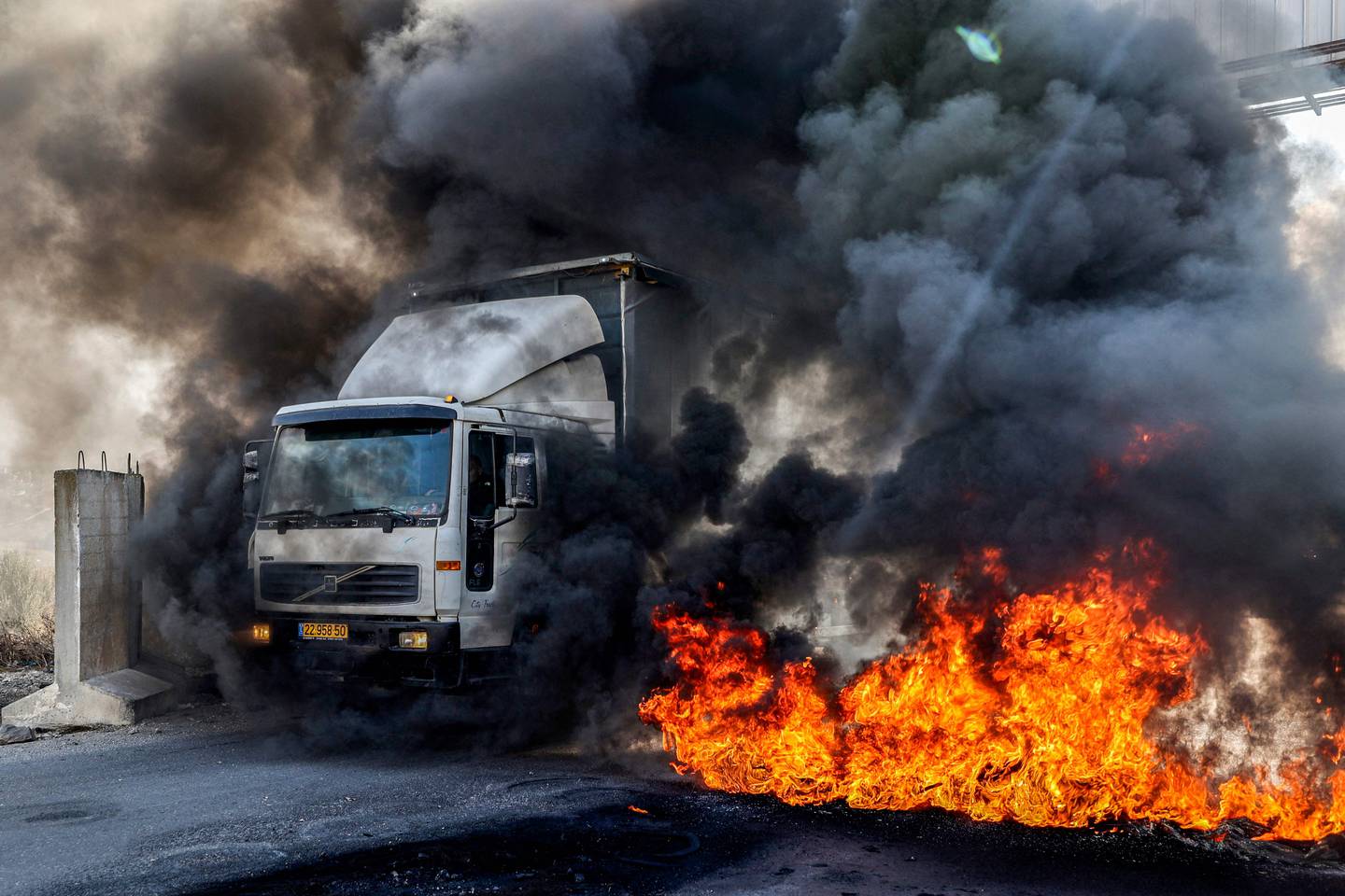 En lastebil på vei mot Nablus kjøer forbi brennende dekk ved sjekkpunktet ved Hawara på Vestbredden. Palestinere protesterer mot at flere veier i området er sperret.