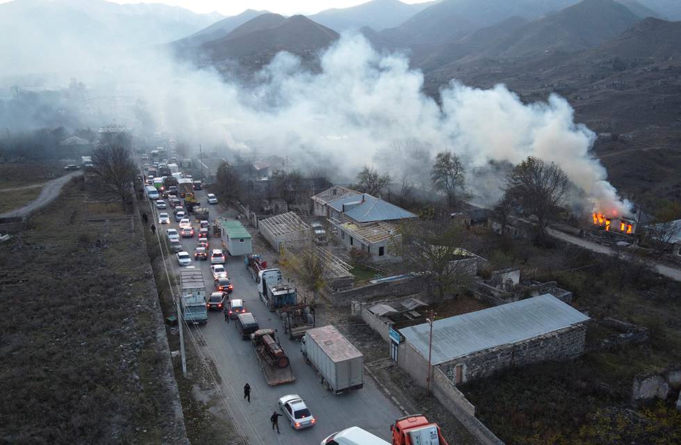 Smoke rises from a burning house as cars and trucks stuck in a huge traffic jam climbing along the road from Kalbajar leaving the separatist region of Nagorno-Karabakh to Armenia, on Saturday, Nov. 14, 2020. The territory is to be turned over to Azerbaijan on Sunday as part of territorial concessions in an agreement to end six weeks of intense fighting with Armenian forces. Hundreds of thousands of Azeris were displaced by the war that ended in 1994. It is unclear when any civilians might try to settle in Karvachar  which will now be known by its Azeri name Kalbajar  or elsewhere. (AP Photo/Dmitry Lovetsky)