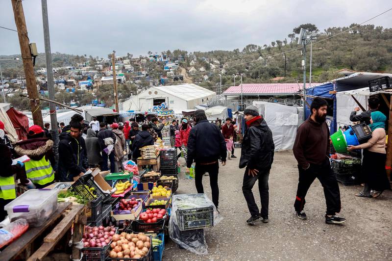 Migrants and refugees walk past fruits and vegetables stalls in a makeshift camp next to the Moria camp on the Greek island of Lesbos on April 2, 2020. - Over 20 coronavirus cases were found in a camp near Athens this week. At the camp of Moria on the island of Lesbos, both doctors and migrants say health precautions are not much help in a facility that is so badly overcrowded. The novel coronavirus could spread faster in overcrowded refugee and displaced persons camps than it has anywhere else so far, warned the International rescue Committee. (Photo by Manolis LAGOUTARIS / AFP)