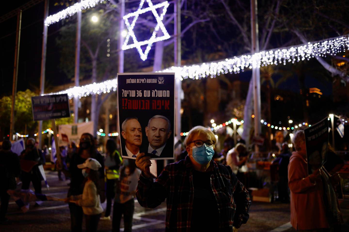 A woman holds a poster of Israeli Prime Minister Benjamin Netanyahu, right, and Benny Gantz, left, that reads: "a government with 36 ministers? Where is the shame?" during a protest against the government and the corruption, at Rabin square, in Tel Aviv, Israel, Saturday, May 2, 2020. Several thousand Israelis took to the streets on Saturday night, demonstrating against Prime Minister Benjamin Netanyahu's new coalition deal with his chief rival a day before the country's Supreme Court is to begin debating a series of legal challenges to the agreement.(AP Photo/Ariel Schalit)