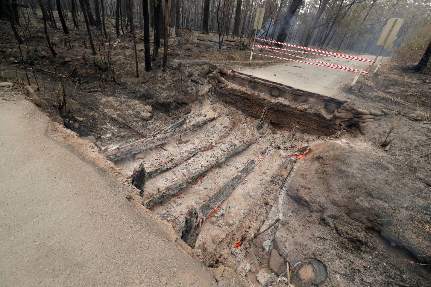 Timbers from a small bridge smolder after fire destroyed the crossing near Burrill Lake, Sunday, Jan. 5, 2020. Milder temperatures Sunday brought hope of a respite from wildfires that have ravaged three Australian states, destroying almost 2,000 homes. (AP Photo/Rick Rycroft)
