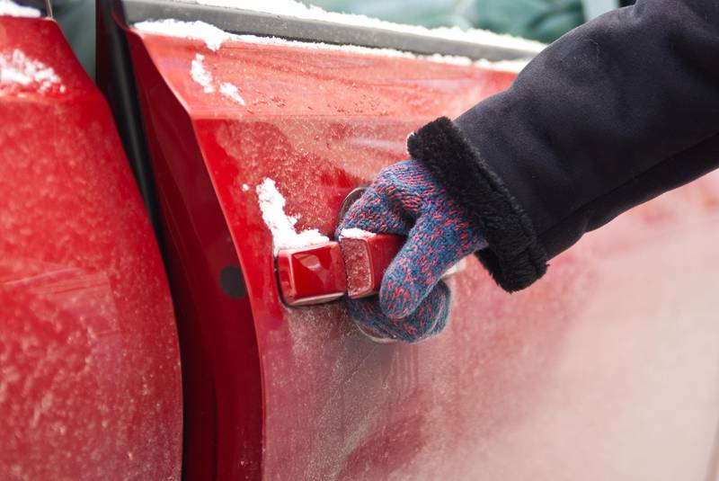 Woman in mitten opens a car door in winter