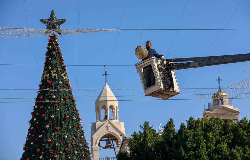 A worker installs decorations next to a giant Christmas tree set in front of the Church of the Nativity compound in Bethlehem in the Israeli-occupied West Bank on December 3, 2020. - Bethlehem is preparing to celebrate the Christmas season under Covid-19 restrictions without the mass of believers and tourists who are usually coming to participate in the annual celebrations.  Before the pandemic, dozens of buses carrying pilgrims and other visitors would converge on the city each day from nearby Jerusalem through the towering Israeli-built grey concrete wall that encircles the West Bank. (Photo by Emmanuel DUNAND / AFP)