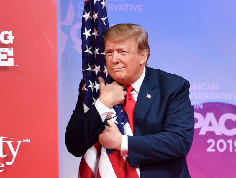 TOPSHOT - US President Donald Trump hugs the US flag as he arrives to speak at the annual Conservative Political Action Conference (CPAC) in National Harbor, Maryland, on March 2, 2019. (Photo by NICHOLAS KAMM / AFP) / ALTERNATIVE CROP