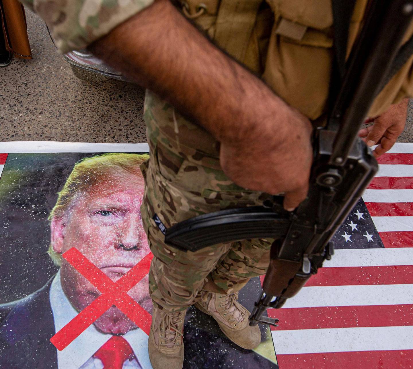En soldat fra Iraks Hashed al-Shaabi-milits står på et bilde av USAs president Donald Trump. Iraks nasjonalforsamling krever nå at USA trekker sine styrker ut av landet.