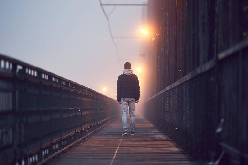 Gloomy weather. Lonely man is walking on the old bridge in mysterious fog.