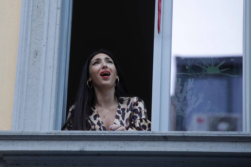 Opera singer Laura Baldassari leans out of her window to sing during a flash mob launched throughout Italy to bring people together and try to cope with the emergency of coronavirus, in Milan, Italy, Friday, March 13, 2020. Italians have been experiencing yet further virus-containment restrictions after Premier Giuseppe Conte ordered restaurants, cafes and retail shops closed after imposing a nationwide lockdown on personal movement. For most people, the new coronavirus causes only mild or moderate symptoms. For some it can cause more severe illness. (AP Photo/Luca Bruno)