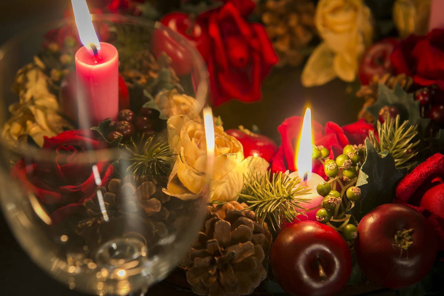 Nærbilde av julekrans med levende lys, et vinglass står foran