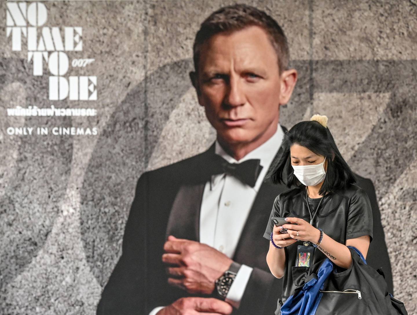 (FILES) In this file photo taken on February 28, 2020, a woman wearing a facemask amid fears of the spread of the COVID-19 novel coronavirus walks past a poster for the new James Bond movie "No Time to Die" in Bangkok. - New James Bond film "No time to die" release is delayed to November after virus fears according to the studio. (Photo by Mladen ANTONOV / AFP)