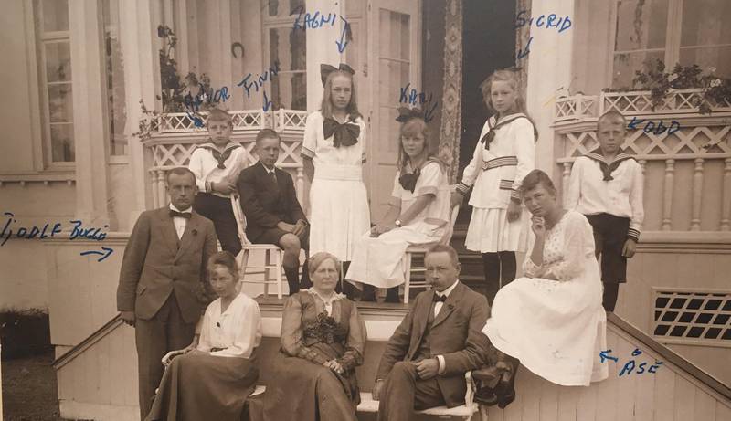 Familien Friis anno 1918: Karoline og Finn A. Friis på hagebenken, omgitt av sine åtte barn og foreløpig ene svigersønn. Det gamle fotoet har påskrevet håndskrift med navnene; Halvor, Finn, Ragni, Kari, Sigrid, Odd og Åse, Gunvor og Tjodolf Bugge.