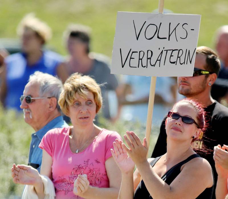 Ikke alle ønsker flyktningene velkommen. Denne kvinnen demonstrerer mot Angela Merkels besøk til et flyktningmottak i Heidenau sist uke. «Folkets forræder» står det på kvinnens plakat. FOTO: NTB SCANPIX