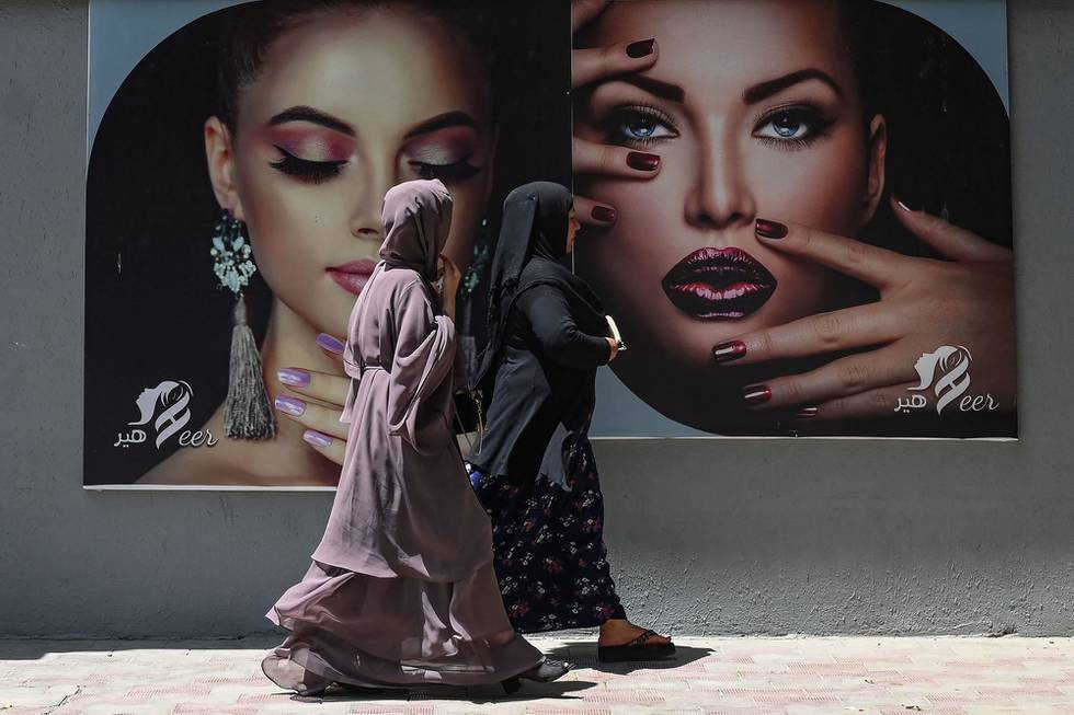 Burkakledde kvinner passerte plakater utenfor en skjønnhetssalong i Kabul 7. august. Nå er flere slike plakater blitt malt over, etter Taliban inntog i hovedstaden.