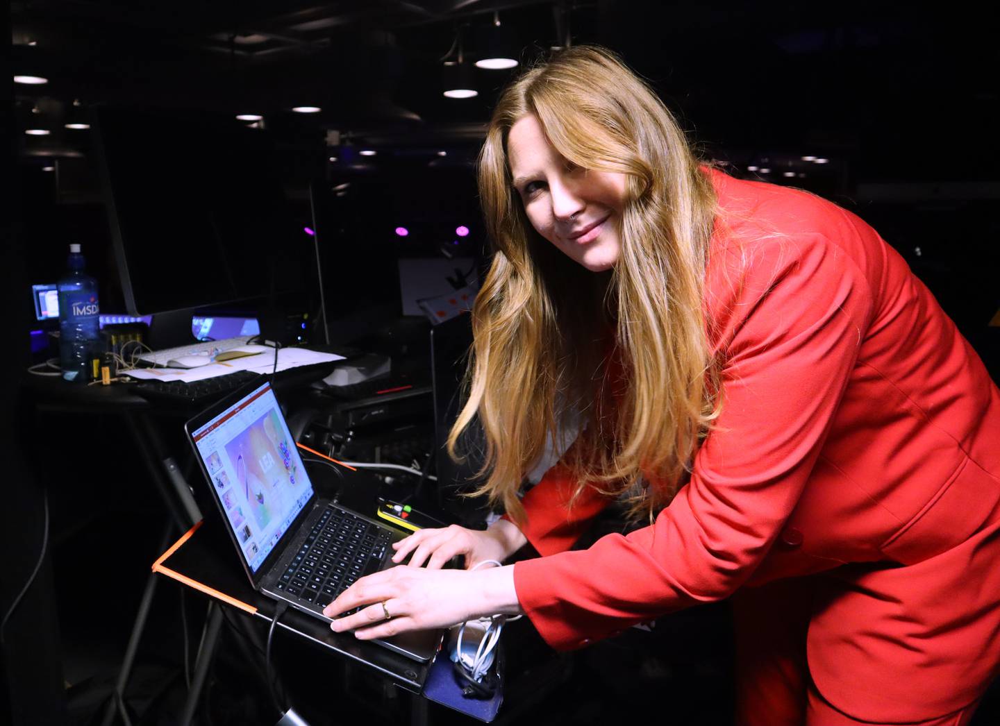 A woman in a pink suit bends over a computer.