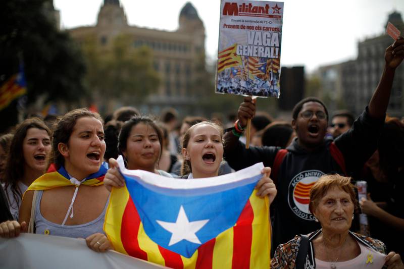 People wearing yellow ribbons in support of jailed pro-independence politicians and carrying Estelada pro-independence flags protest in Barcelona, Spain, Monday, Oct. 14, 2019. Spain's Supreme Court on Monday convicted 12 former Catalan politicians and activists for their roles in a secession bid in 2017, a ruling that immediately inflamed independence supporters in the wealthy northeastern region. Poster reads in Catalan, General Strike. (AP Photo/Emilio Morenatti)