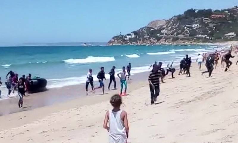 En kvinne ser på mens en gruppe migranter og flyktninger går i land fra en gummibåt på stranda i Cádiz i Sør-Spania. Bildet er tatt fra en video.