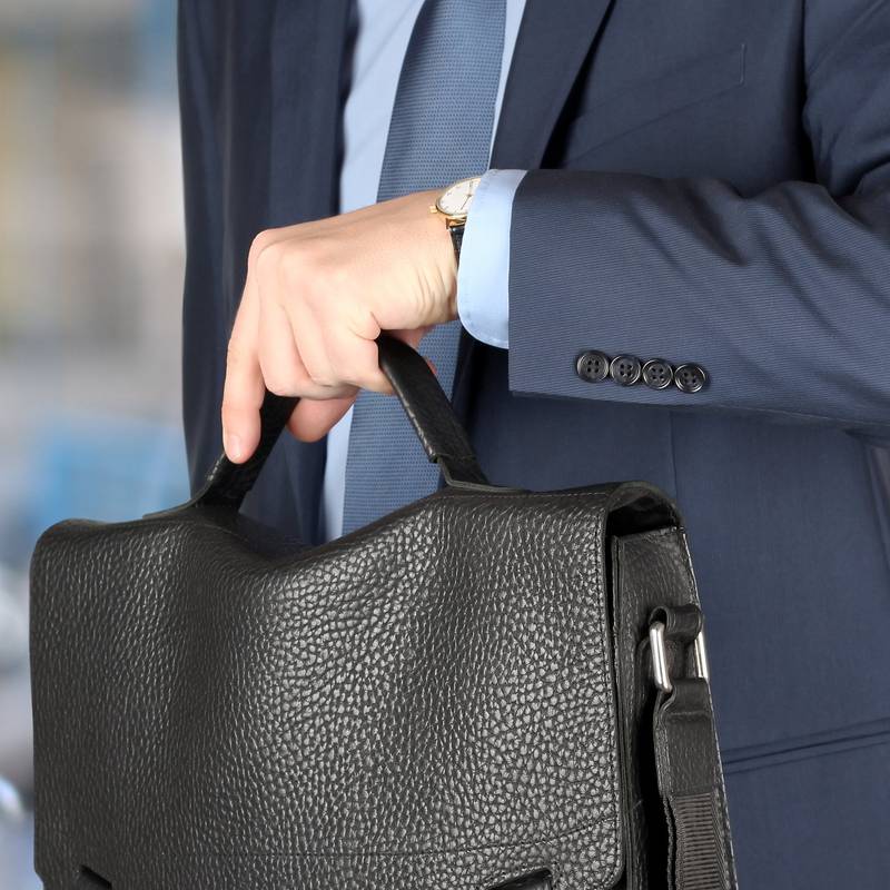 businessman  holding leather briefcase checking time on his watch at the airport.