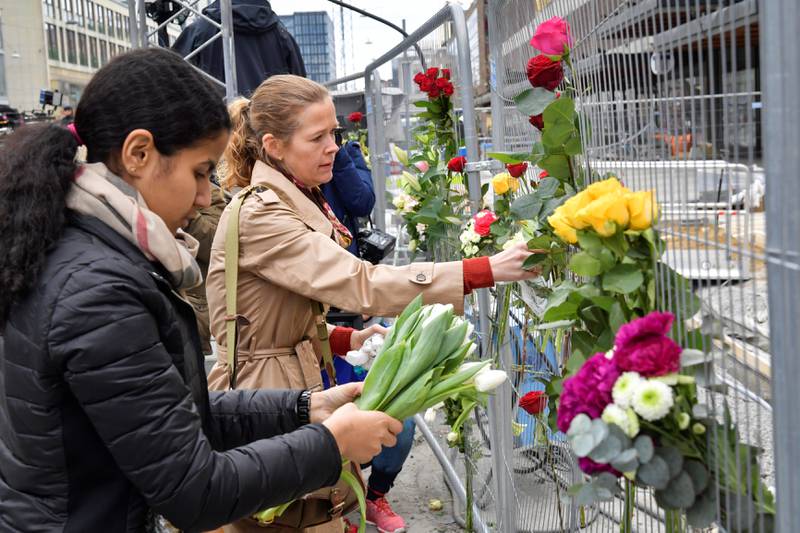 BLOMSTER: Folk legger ned blomster i nærheten av stedet der en lastebil braste inn i et varehus og drepte fire mennesker fredag ettermiddag i Stockholm.