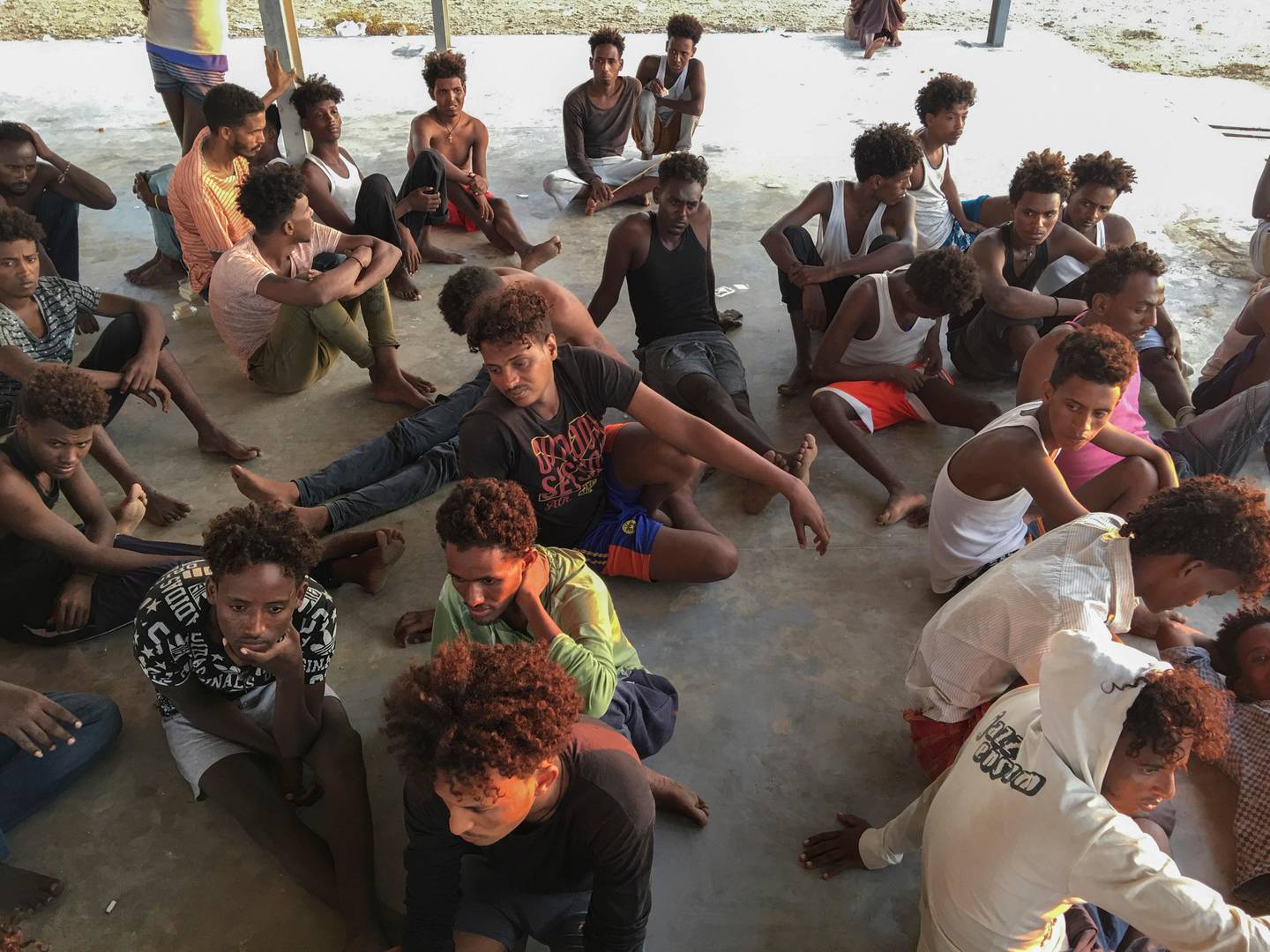 Rescued migrants sit on a coast some 100 kilometers (60 miles) east of Tripoli, Libya, Thursday, July 25, 2019. The U.N. refugee agency and the International Rescue Committee say up to 150 may have perished at sea off the coast of Libya. The country's coast guard says the Europe-bound migrants are missing and feared drowned after the boats they were traveling on capsized in the Mediterranean Sea. A spokesman says they rescued around 137 migrants on Thursday. (AP Photo/Hazem Ahmed)