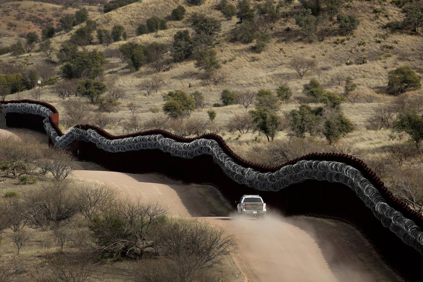 FILE - This March 2, 2019, file photo, shows a Customs and Border Control agent patrolling on the US side of a razor-wire-covered border wall along the Mexico east of Nogales, Ariz. A border activist charged with helping a pair of migrants with water, food and lodging is set to go on trial in U.S. court in Arizona. Defendant Scott Daniel Warren has argued that his spiritual values compel him to help all people in distress. The trial is scheduled to begin Wednesday, May 29, 2019, in Tucson, with the 36-year-old Warren charged with harboring migrants and conspiring to transport and harbor two Mexican men found with him who were in the U.S. illegally. (AP Photo/Charlie Riedel, File)