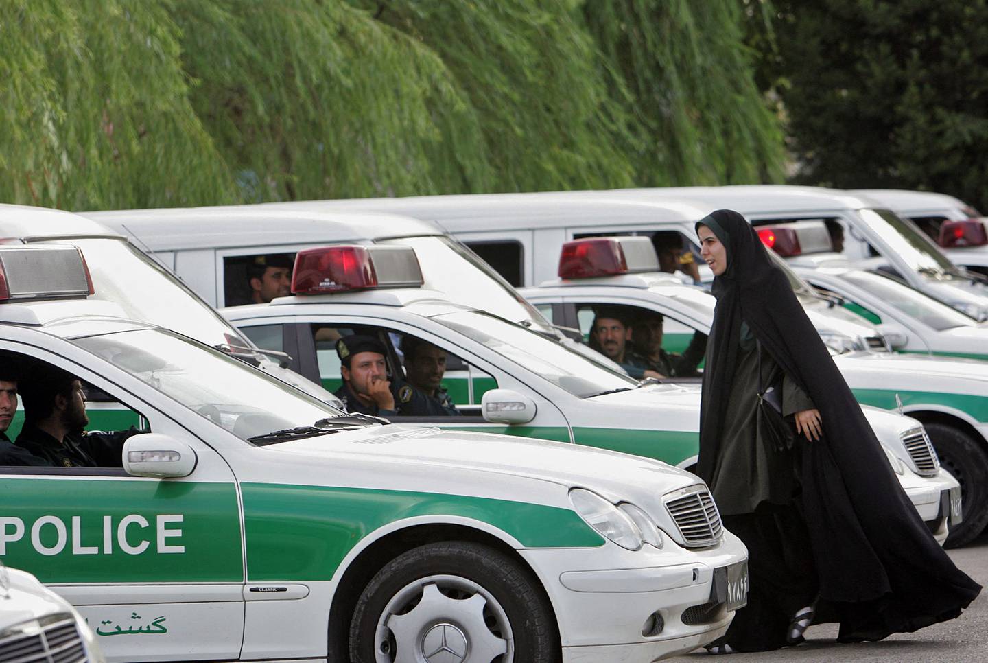 Et kvinnelig medlem av det iranske moralpolitiet går mellom biler som tilhører politistyrken i Teheran i 2007.