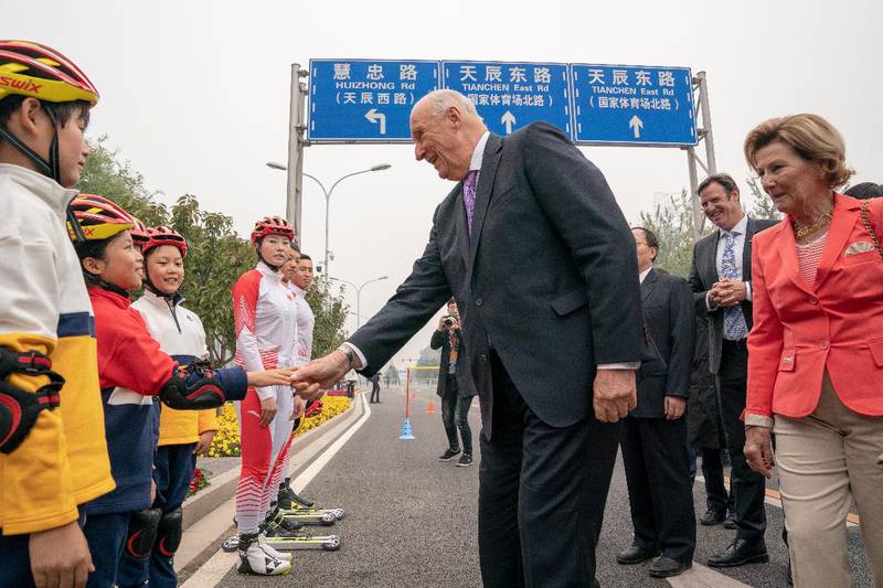 Kong Harald og dronning Sonja hilser på unge kinesiske rulleskiutøvere utenfor Beijings mest berømte friidrettsstadion, Fugleredet i Beijing mandag. Norges idrettspresident Tom Tvedt i bakgrunnen.