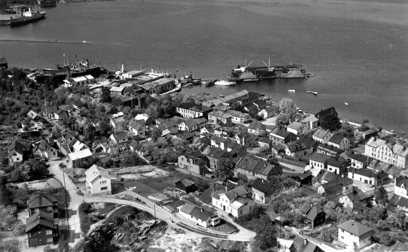 bebyggelse på Tangen 1952: Drammen Slip og Verksted i bakgrunnen, og Peter Høeg seilmakeri nede ved fjorden. I Iversbakken står beboerne og speider opp mot Widerøe-flyet.