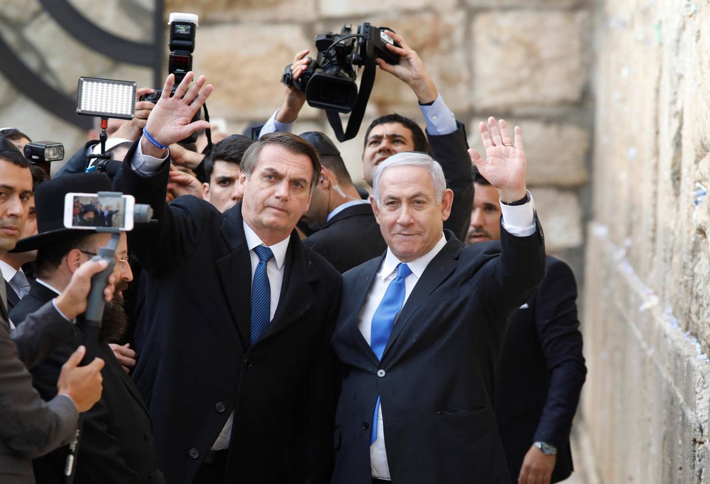 Brazilian President Jair Bolsonaro, left, and Israeli Prime Minister Benjamin Netanyahu wave to journalists during a visit to the Western wall, the holiest site where Jews can pray, in the Old City of Jerusalem, Monday, April 1, 2019.  (Menahem Kahana/Pool Photo via AP)