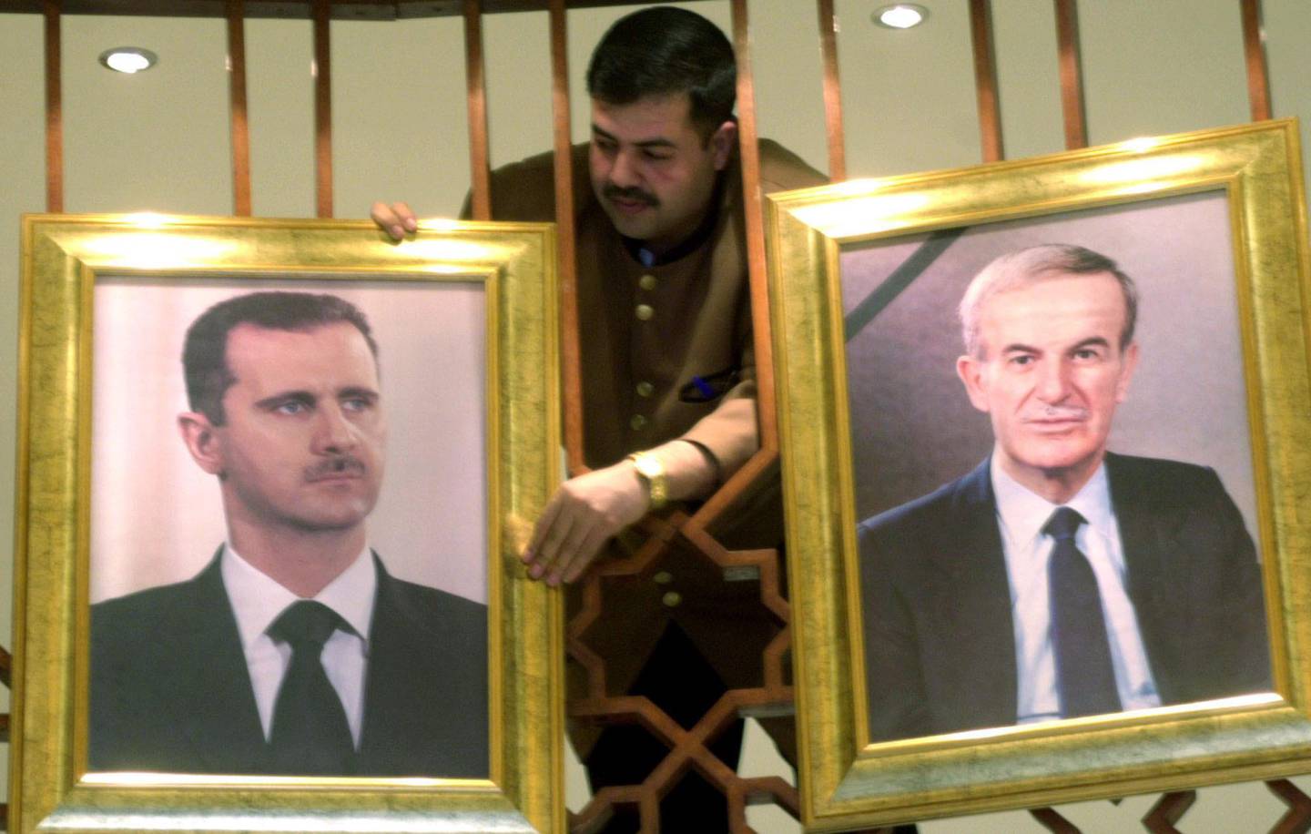 a Syrian worker at a Damascus hotel, hangs on Saturday, March. 5, 2005 two big photos, one of President Bashar Assad, left,  and of his father, late President  Hafez Assad. Bashar Assad is scheduled to deliver a speech to his parliament later in the day, in which he is expected to announce a troops withdrawal from Lebanon to the Bekaa region in eastern Lebanon.(AP Photo Bassem Tellawi).