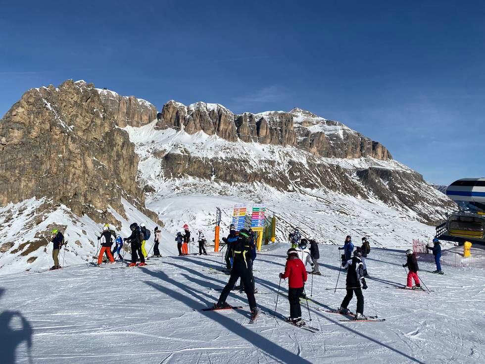 Mennesker står på toppen av slalåmbakken med Dolomittene i bakgrunnen.
