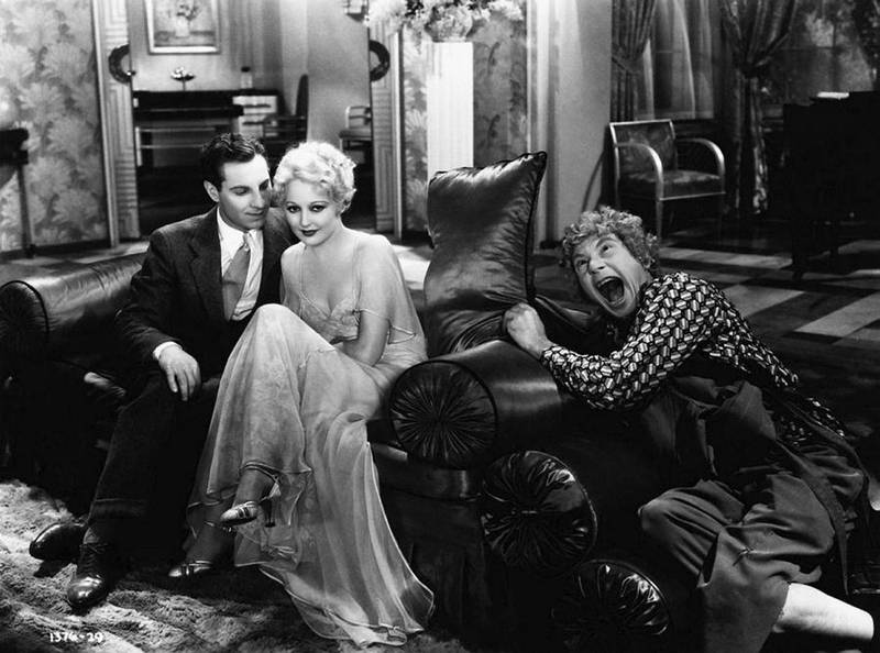 Zeppo Marx sitter sammen med Thelma Todd i en sofa mens Harpo Marx har et raserianfall ved siden av i denne scenen fra «Horse Feathers» (1932).
