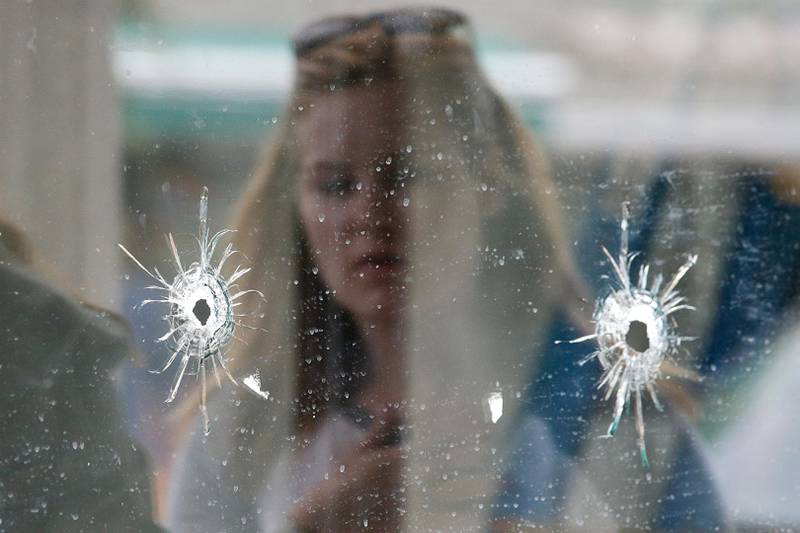 FILE- In this May 24, 2014, file photo, a woman looks at the bullet holes on the window of IV Deli Mark where a mass shooting took place near the University of California, Santa Barbara campus, in the Isla Vista beach community. In response to the killing rampage of Elliot Rodger, 22, that left seven people, including himself dead, lawmakers approved and California Gov. Jerry Brown signed a law which requires law enforcement agencies to develop policies that encourage officers to search the state's database of gun purchases as part of routine welfare checks. More than 900 laws approved by the Legislature and signed by the governor will take effect Jan. 1, 2015. (AP Photo/Jae C. Hong, File)