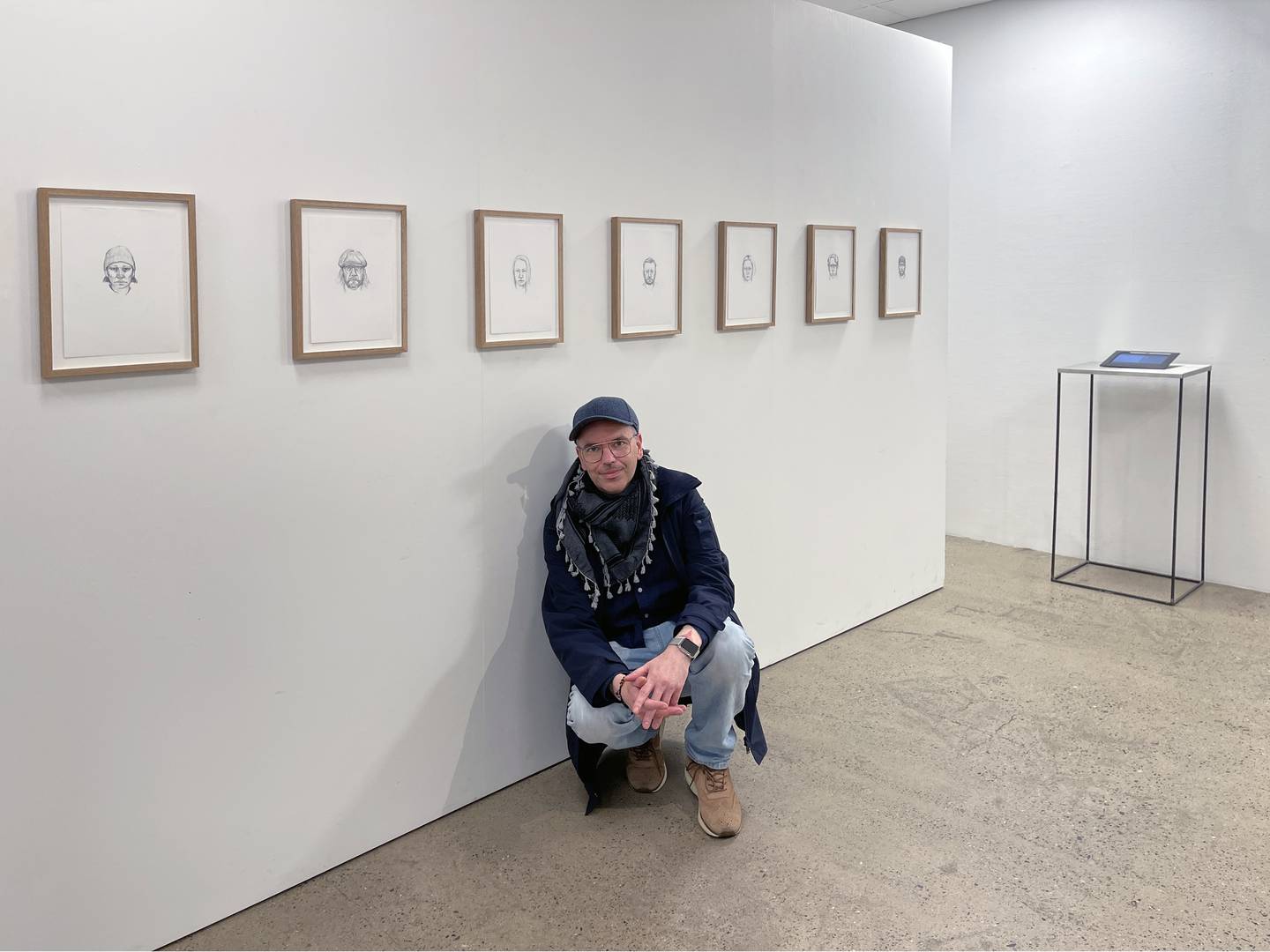 Kunstner Anders Eiebakke poserer foran en gallerivegg med innrammede tegninger.