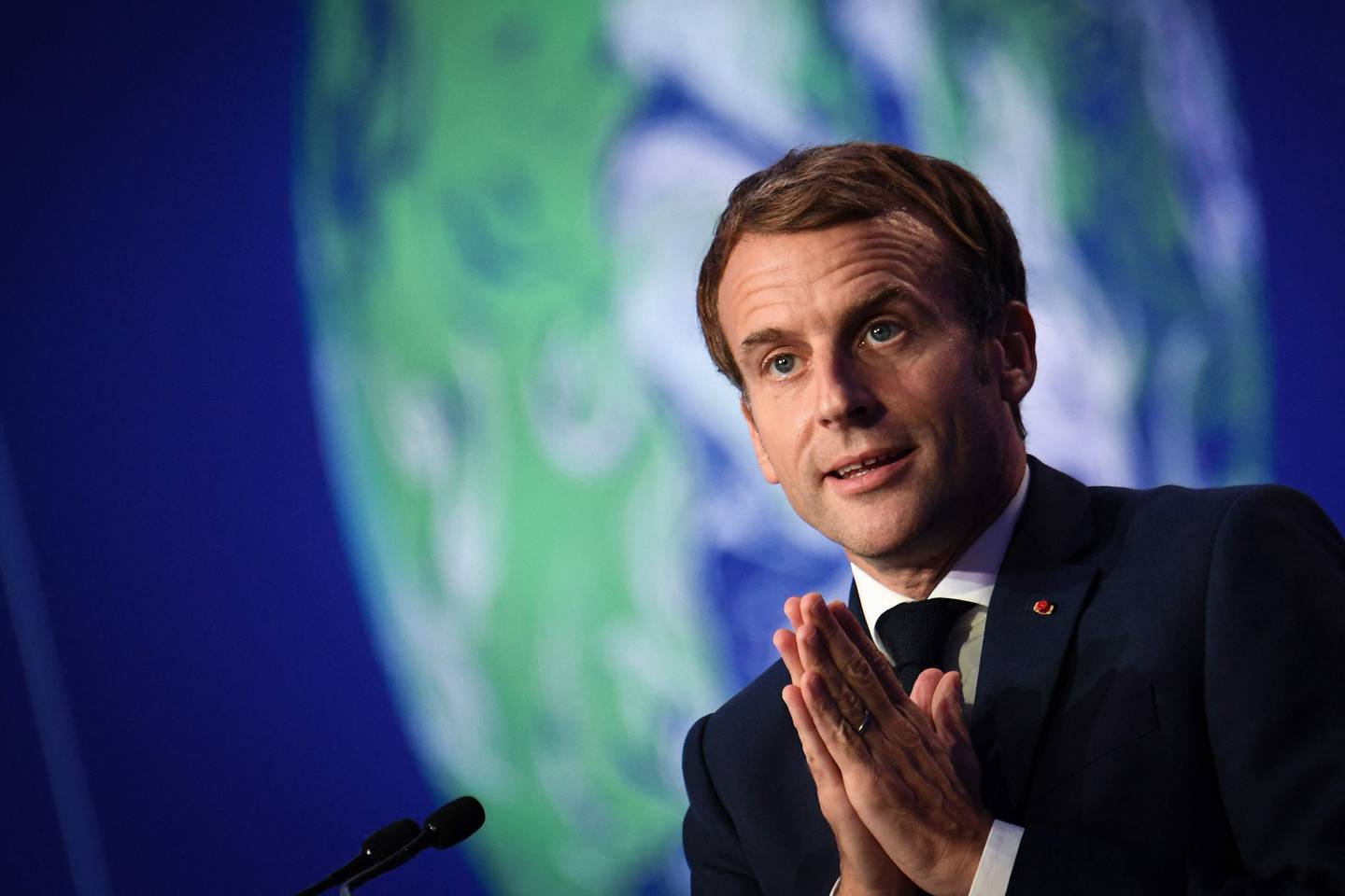 President Emmanuel Macron står med hendene foldet foran seg mens han snakker til de oppmøtte på klimakonferansen COP26.
