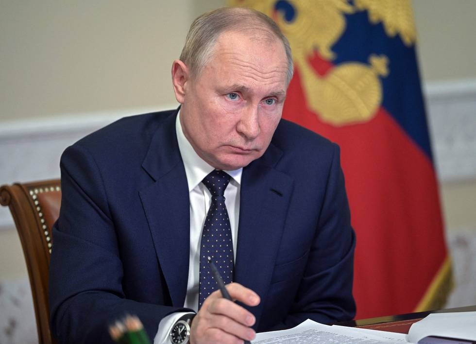 Russlands president Vladimir Putin lyttende med en penn i hånda og papirer foran seg på en pult