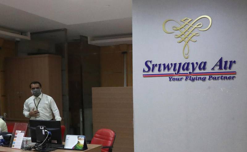 A staff member near Sriwijaya Air logo at their ticketing office at Soekarno-Hatta International Airport in Tangerang, Indonesia, Saturday, Jan. 9, 2021. A Sriwijaya Air passenger jet with 56 passengers and six crew members onboard, lost contact with air traffic controllers after taking off from Indonesia's capital on Saturday on a domestic flight, officials said. (AP Photo/Tatan Syuflana)