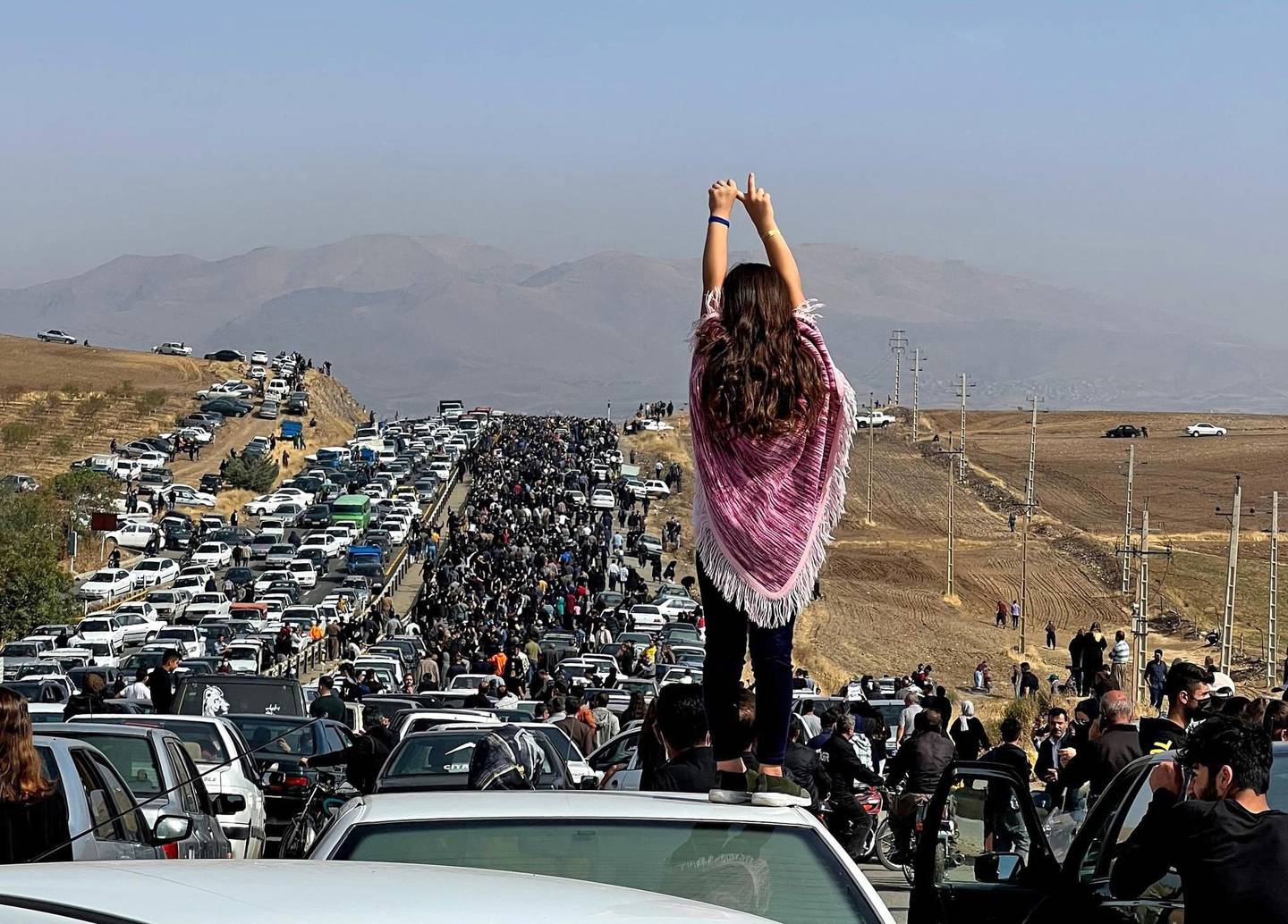 En kvinne står på et biltak mens tusenvis av demonstranter går mot en gravlund i Mahsa Aminis hjemby i Iran for å markere at det var 40 dager siden hun døde.